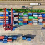 A top-down view of shipping containers stacked near a freeway