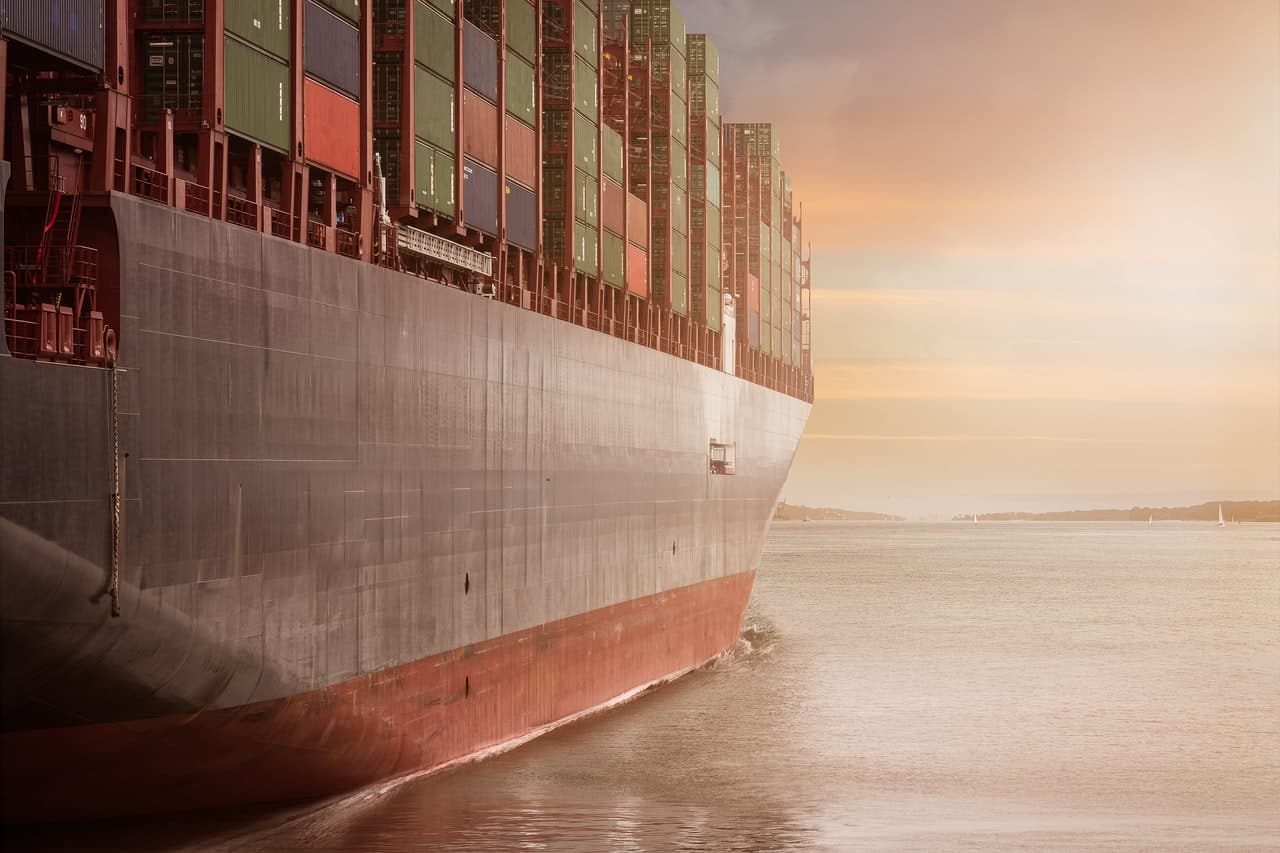 A freighter filled with cargo containers sailing toward the sunset.