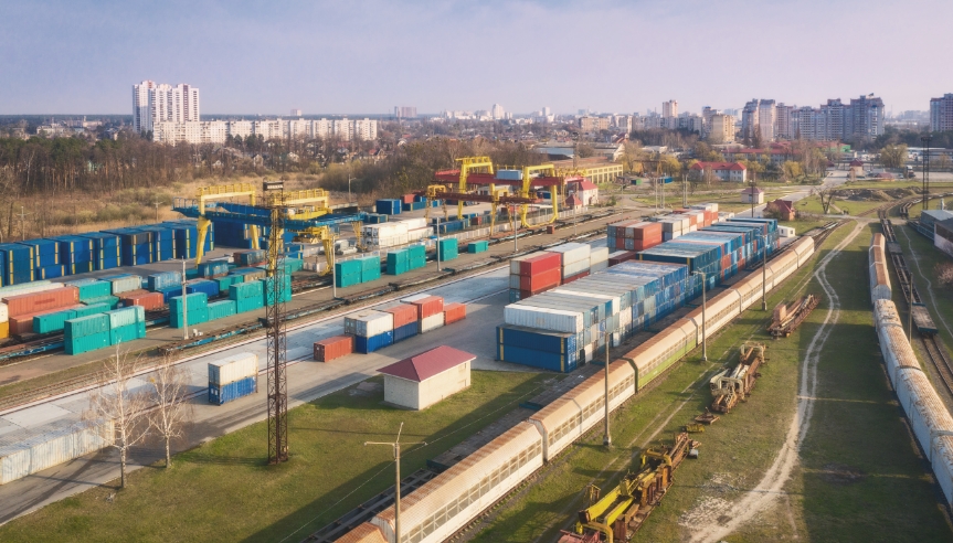 A photo of a shipping yard with trains in the foreground and shipping containers in the background.